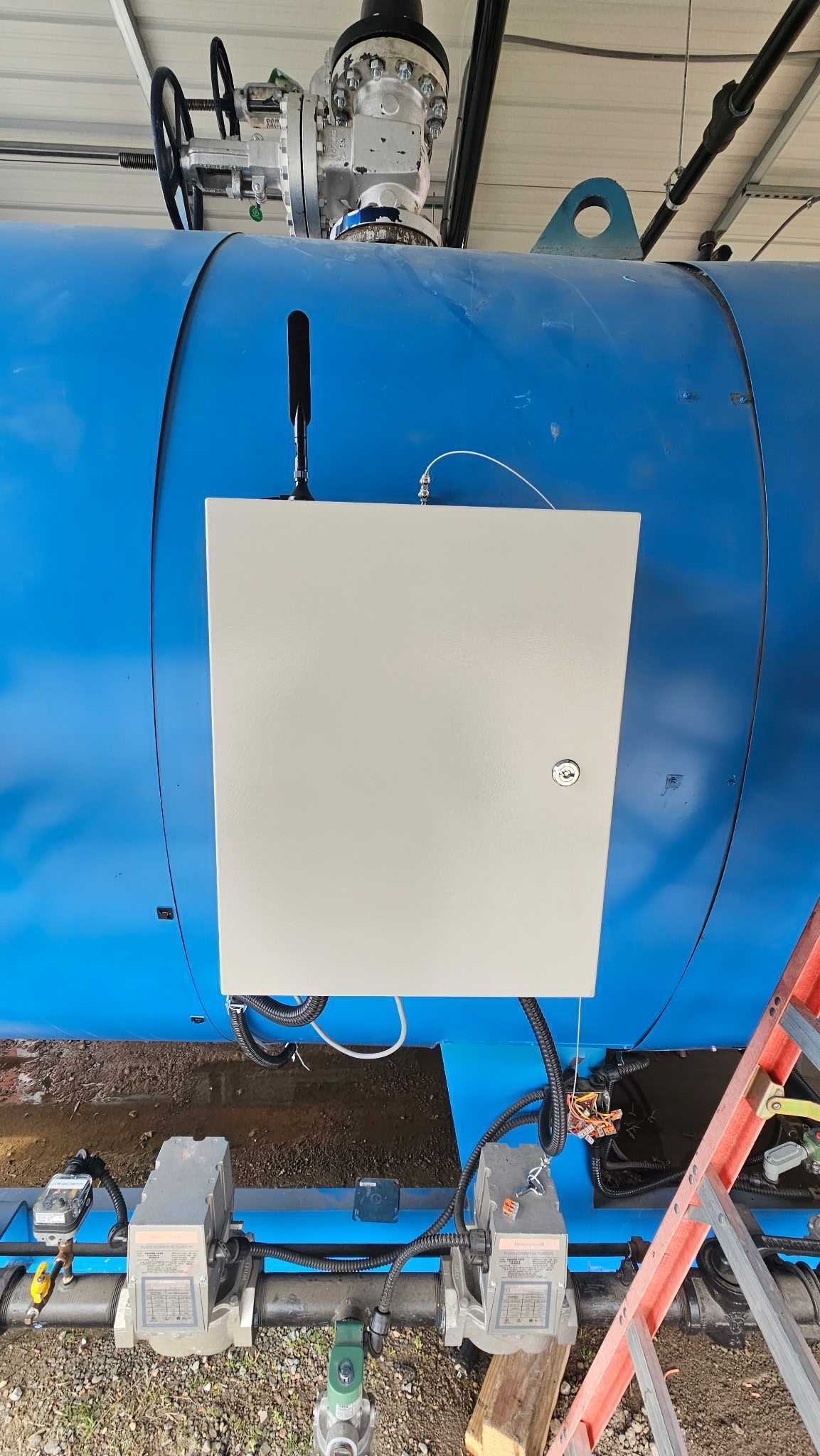 A Squawkbox cellular monitoring enclosure with antenna mounted on an industrial blue boiler